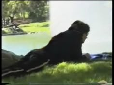 a man laying in the grass next to a body of water