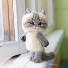 a stuffed animal cat sitting on top of a window sill next to a window