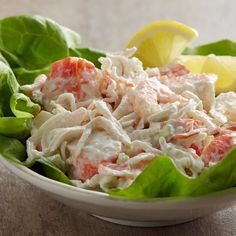 a salad in a white bowl with lettuce and lemon wedges on the side