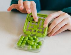 a child playing with green candies in a container on the table, while someone is reaching for them