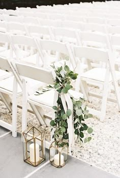 two white chairs with greenery tied to them and candles on the ground in front of them