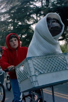 two people riding bikes down a street with a monkey on it's back and another person wearing a red hoodie