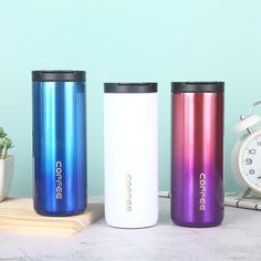 three stainless steel tumblers sitting on top of a table next to an alarm clock