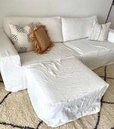 a white sectional couch with pillows on top of it and a rug in the middle