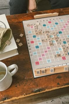 a scrabble board sitting on top of a wooden table next to a cup of coffee