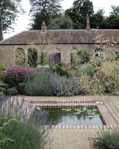 an old brick building with a pond in the middle and lots of plants around it