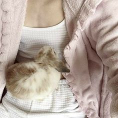 a woman is holding a baby bird in her lap while wearing a white shirt and pink cardigan