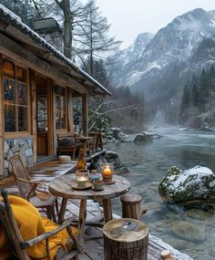 a table and chairs on a deck next to a body of water with mountains in the background