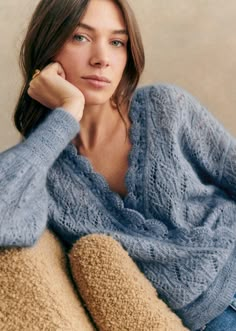 a woman sitting on a couch wearing a blue sweater and jeans with her hand under her chin