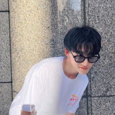 a young man wearing sunglasses leaning against a wall with his hand on the ground and looking down