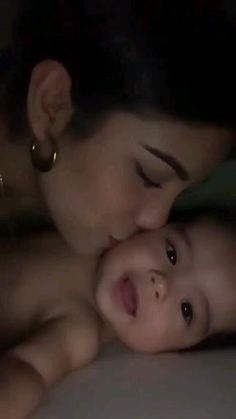 a woman and child laying on top of a bed next to each other in the dark