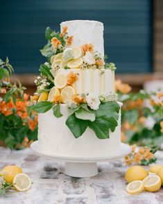 a wedding cake with lemons and greenery on the top is surrounded by flowers