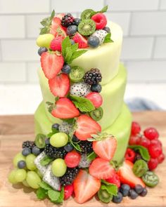 a three tiered cake covered in fresh fruit on top of a wooden cutting board