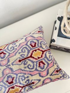 a pillow sitting on top of a white table next to a magazine and a lamp