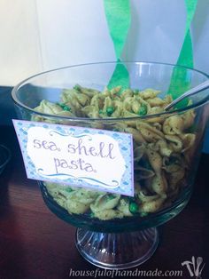 a glass bowl filled with pasta on top of a wooden table next to a sign that says sea shell pasta