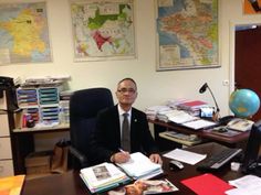 a man sitting at a desk in an office with lots of books and papers on it