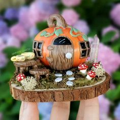 a hand holding up a miniature house made out of wood with mushrooms and mushrooms around it