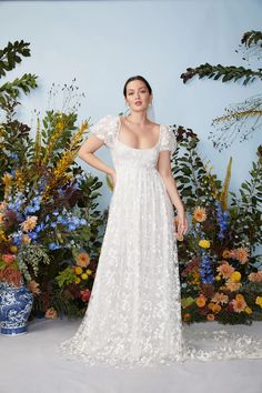 a woman standing in front of flowers wearing a white dress