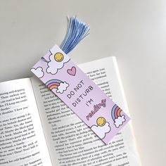 an open book with a blue tassel on top of it next to a pink bookmark