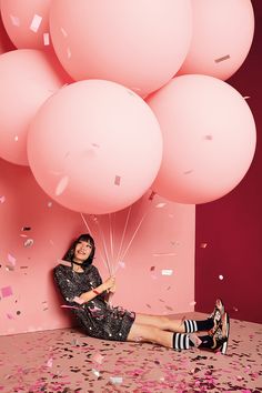 a woman sitting on the floor with balloons and confetti in front of her