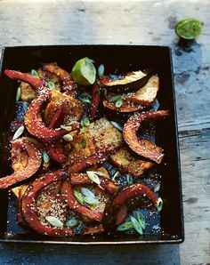 a black plate topped with sliced vegetables and seasoning on top of a wooden table