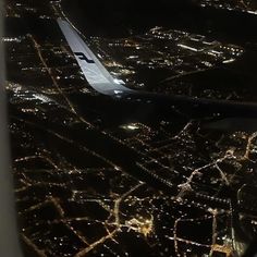 an airplane wing flying over a city at night with lights on the ground and in the air