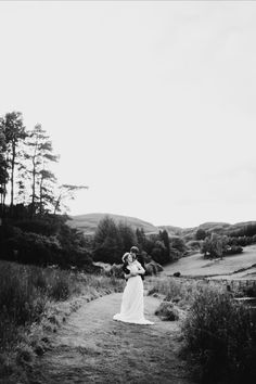 a bride and groom standing in the middle of a path surrounded by tall grass with trees on either side