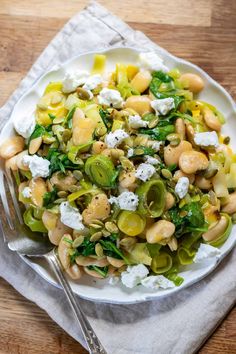 a white plate topped with pasta and veggies next to a fork on top of a wooden table