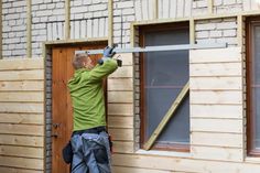 a man in green shirt and black pants working on a house with wooden sidings