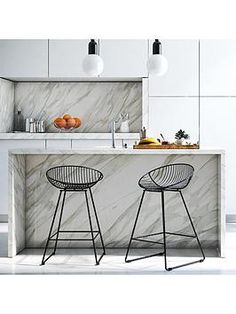 two bar stools sit in front of an island with marble countertops and white cabinets