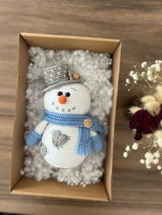 a snowman ornament in a box on a table next to dried flowers