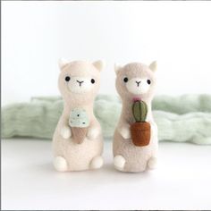 two stuffed llamas are sitting next to each other with a plant in their hands