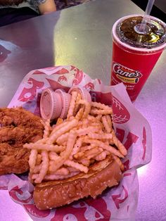 a chicken sandwich and fries on a table with a drink in the background at a fast food restaurant