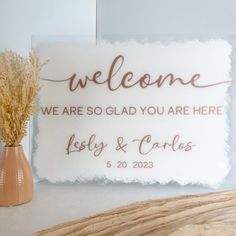 a welcome sign is placed next to a vase with dried grass in it and the words, we are so glad you are here