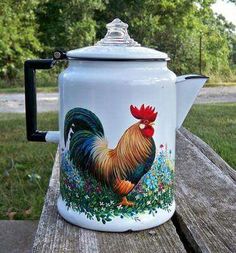 a painted coffee pot sitting on top of a wooden table next to grass and trees