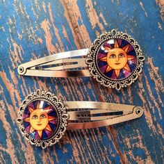 Set of two sun face hair clips in vibrant yellow-gold, blue,  and purple. Antiqued silver setting for a rustic look. Glass cabochons cover the images and are set in antiqued silver tone hair clips. The clip measures almost 2.75" long. Image itself is 20mm. Item is not waterproof. Sun Hair Clip, Hippy Hair, Aesthetic Accessories, Hippie Hair, Sun Face, Rustic Boho, Tone Hair, Face Hair, Barrettes