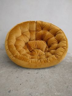 a yellow round chair sitting on top of a cement floor next to a white wall