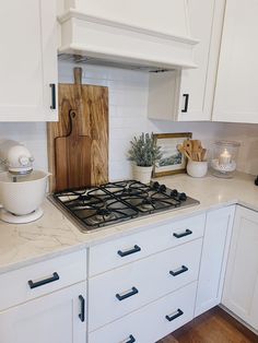 a kitchen with white cabinets and marble counter tops is pictured in this image, there are two cutting boards on the stove top