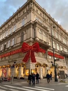 people walking in front of a large building with a red bow on it