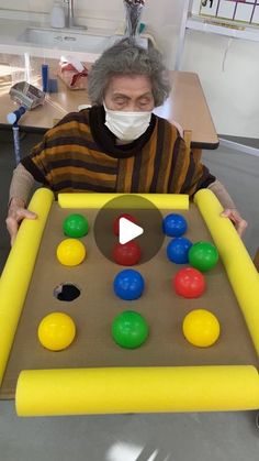 an old woman wearing a face mask playing with balls in a game board while sitting at a table