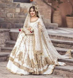 a woman in a white and gold bridal gown standing on steps with her arms around her waist