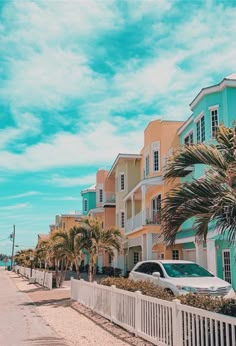 a row of colorful houses on the beach with cars parked along the sidewalk and palm trees lining the street