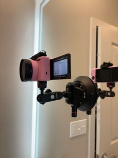 a pink camera attached to a tripod in front of a white door with a mirror behind it