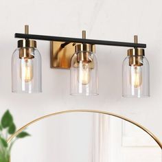 three light bathroom fixture with clear glass shades and gold accents on the wall above it