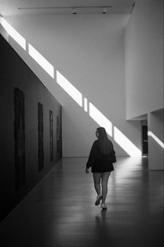 a woman walking down a long hallway in black and white