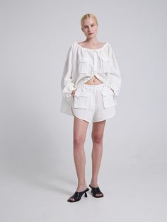 a woman standing in shorts and a white top with ruffles on the sides