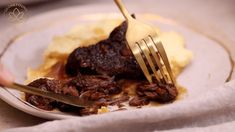 a person is holding a fork and knife over some food on a plate with mashed potatoes