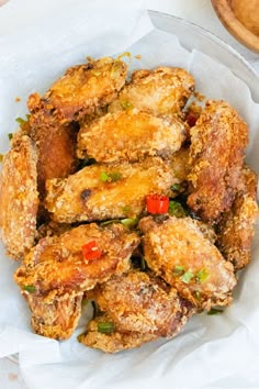 fried chicken wings in a basket on top of a white table cloth next to a wooden bowl