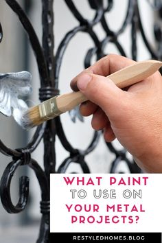 a hand holding a paintbrush near a metal fence with the words, what paint to use on your metal projects?