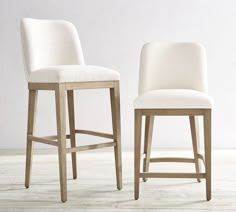 two white bar stools sitting next to each other on a wooden floor in front of a wall